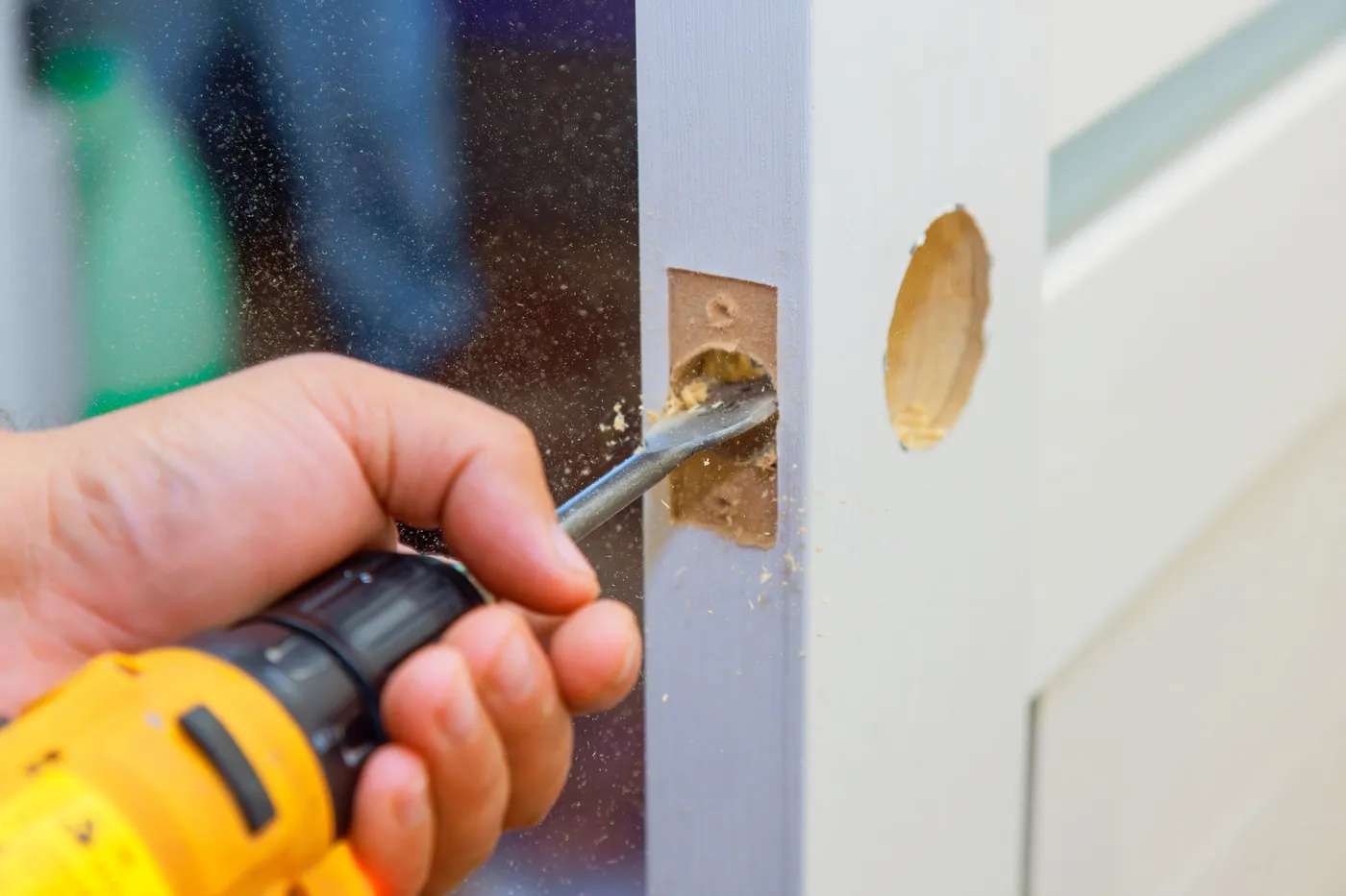 Perçage à la perceuse d'un logement de serrure dans le chant d'une porte près de la place Dupleix dans le 15e arrondissement